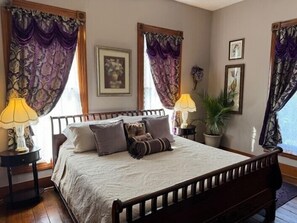 A neatly made bed with a wooden frame, two bedside tables with lamps, and a potted plant on the right.