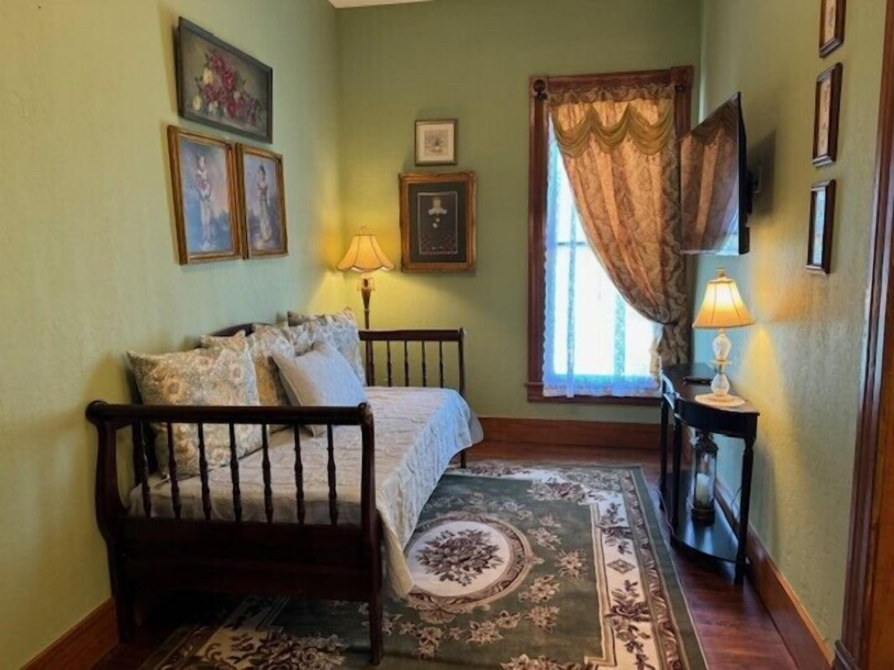 A bedroom with a wooden bed, a patterned rug, a nightstand with a lamp, and framed pictures on the wall.