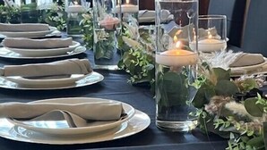 A table set with plates, napkins, and candles, surrounded by greenery and glass candle holders. - Woodbine Inn and Restaurant (Madisonville)