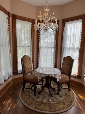 A dining area with a round table, two chairs, a chandelier, and lace curtains. - Woodbine Inn and Restaurant (Madisonville)
