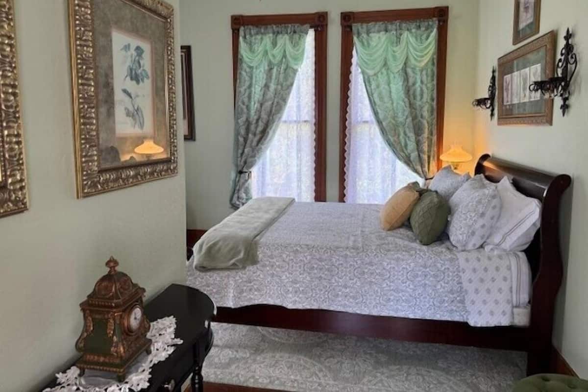 A bedroom with a bed, a nightstand, a clock, and curtains.