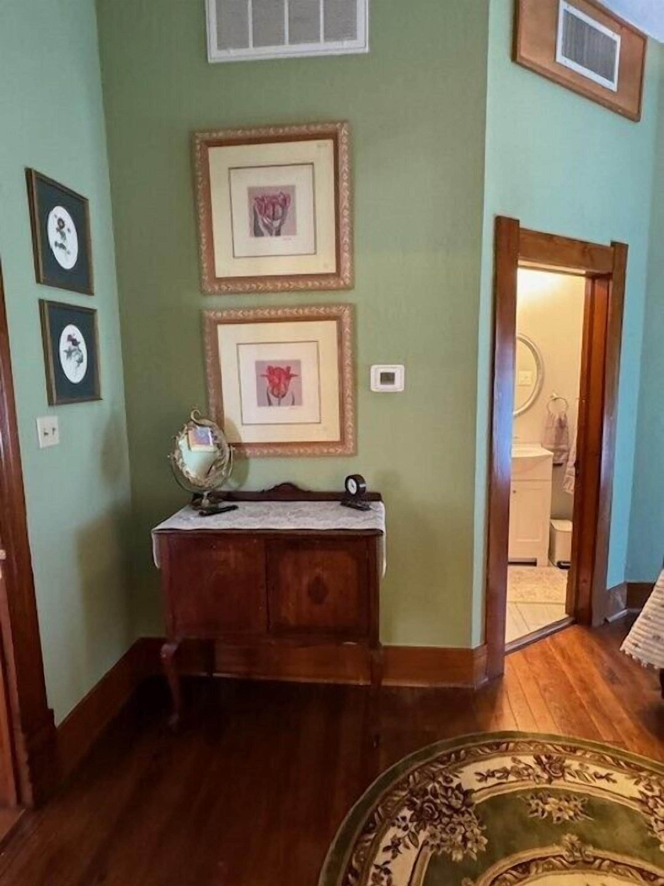 A room with a wooden desk, framed pictures on the wall, and a patterned rug on the floor.