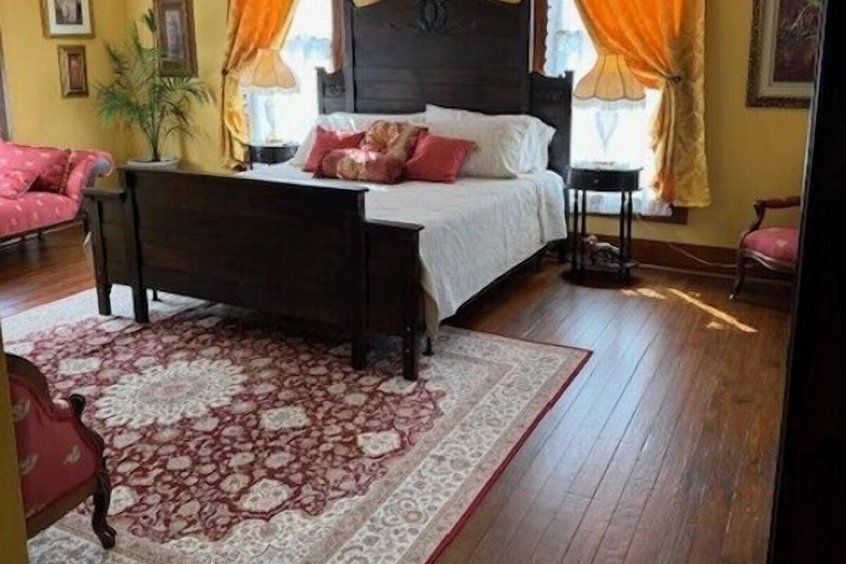 A bedroom with a wooden bed, two nightstands, a large rug, and a ceiling fan.