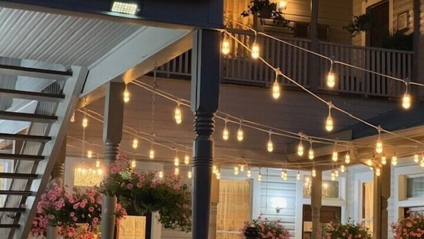 A covered outdoor area with string lights, wooden railings, and hanging flower arrangements. - Woodbine Inn and Restaurant (Madisonville)