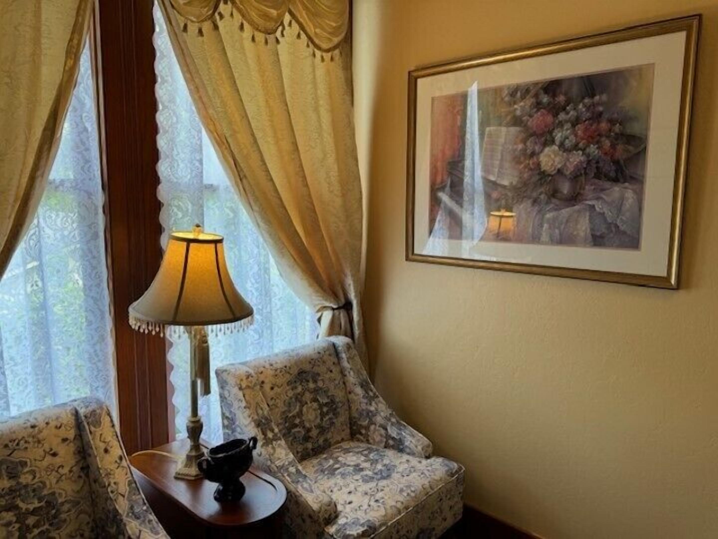 A corner room with a patterned sofa, a table with a lamp, and a framed artwork on the wall.