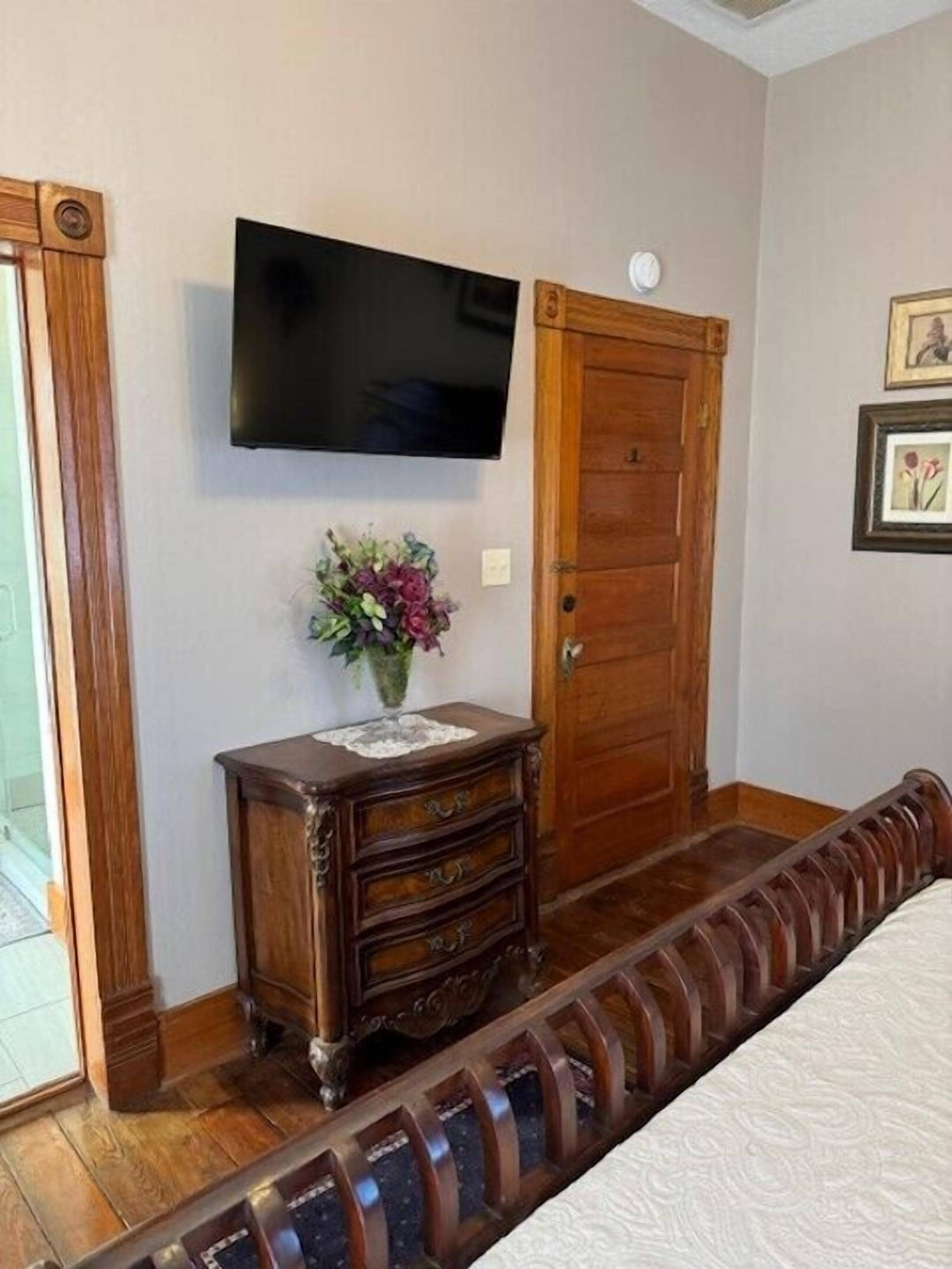 A bedroom with a wooden dresser, a television mounted on the wall, and a door with a decorative handle.