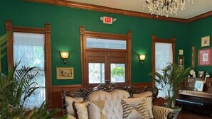 A room with a large, ornate sofa, two wall-mounted lamps, and a chandelier. - Woodbine Inn and Restaurant (Madisonville)