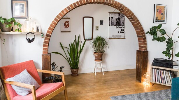 Una sala de estar acogedora con un arco de ladrillo, una silla roja, plantas en macetas y un tocadiscos.