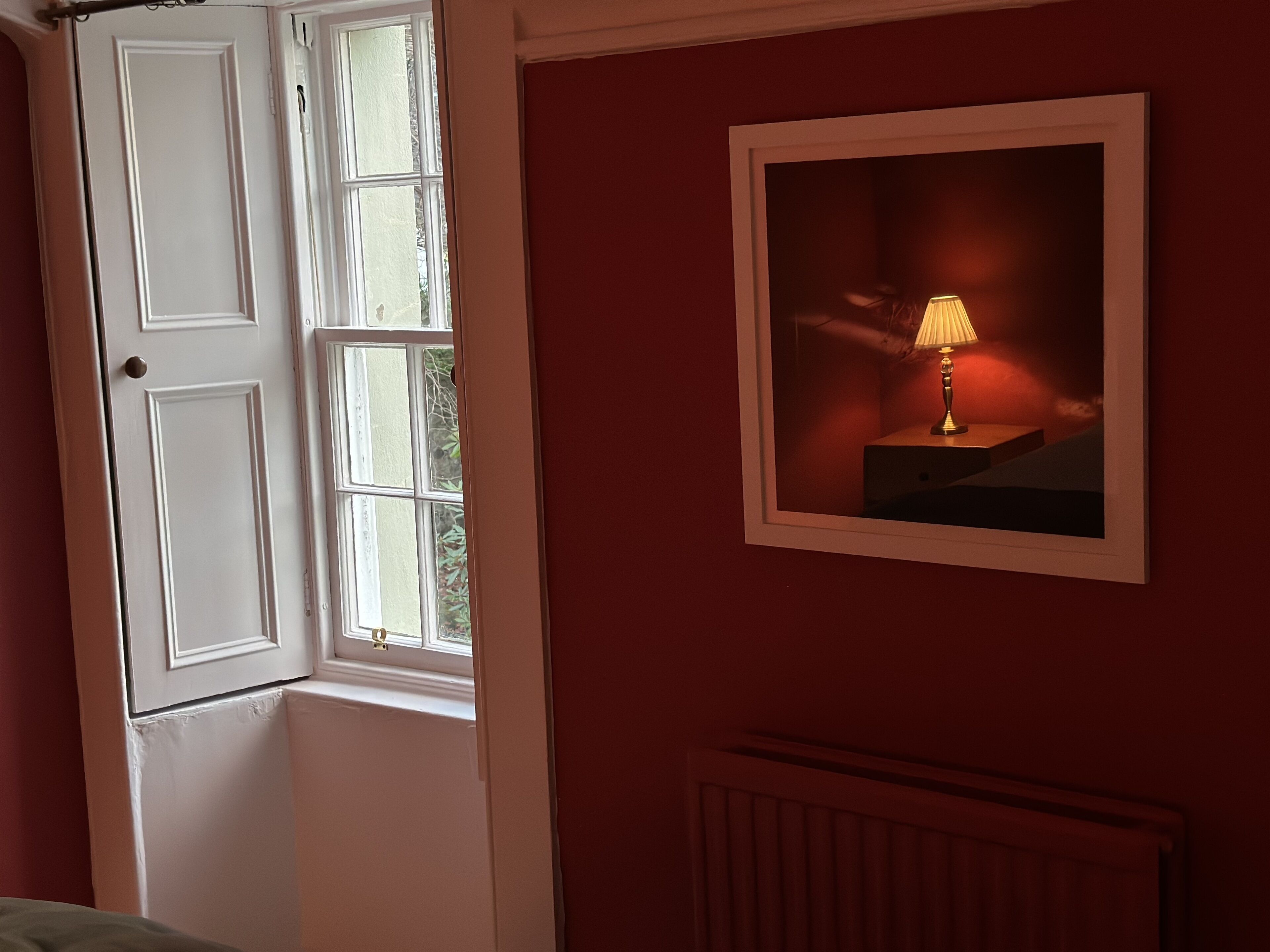 A room with a partially open door, a radiator, and a framed picture of a lamp on the wall.