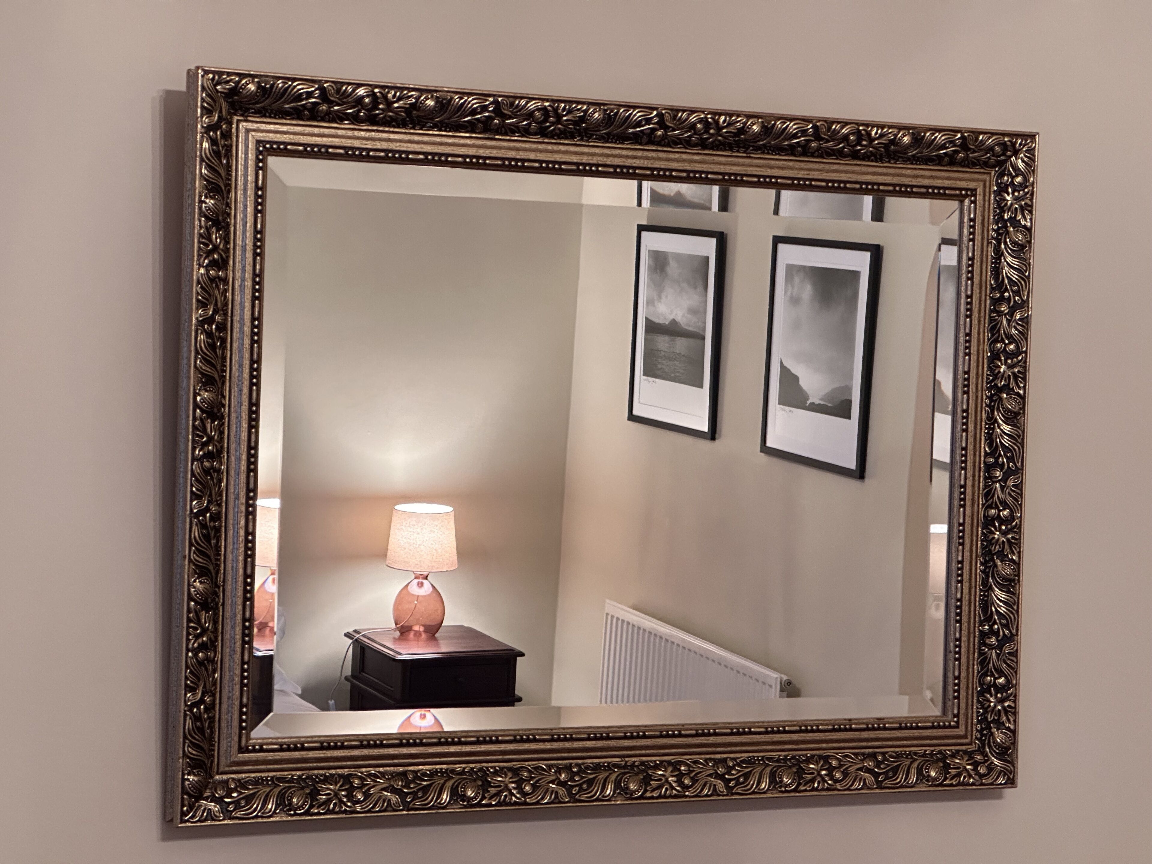 Un miroir avec un cadre orné, une lampe et deux tableaux encadrés accrochés au mur.