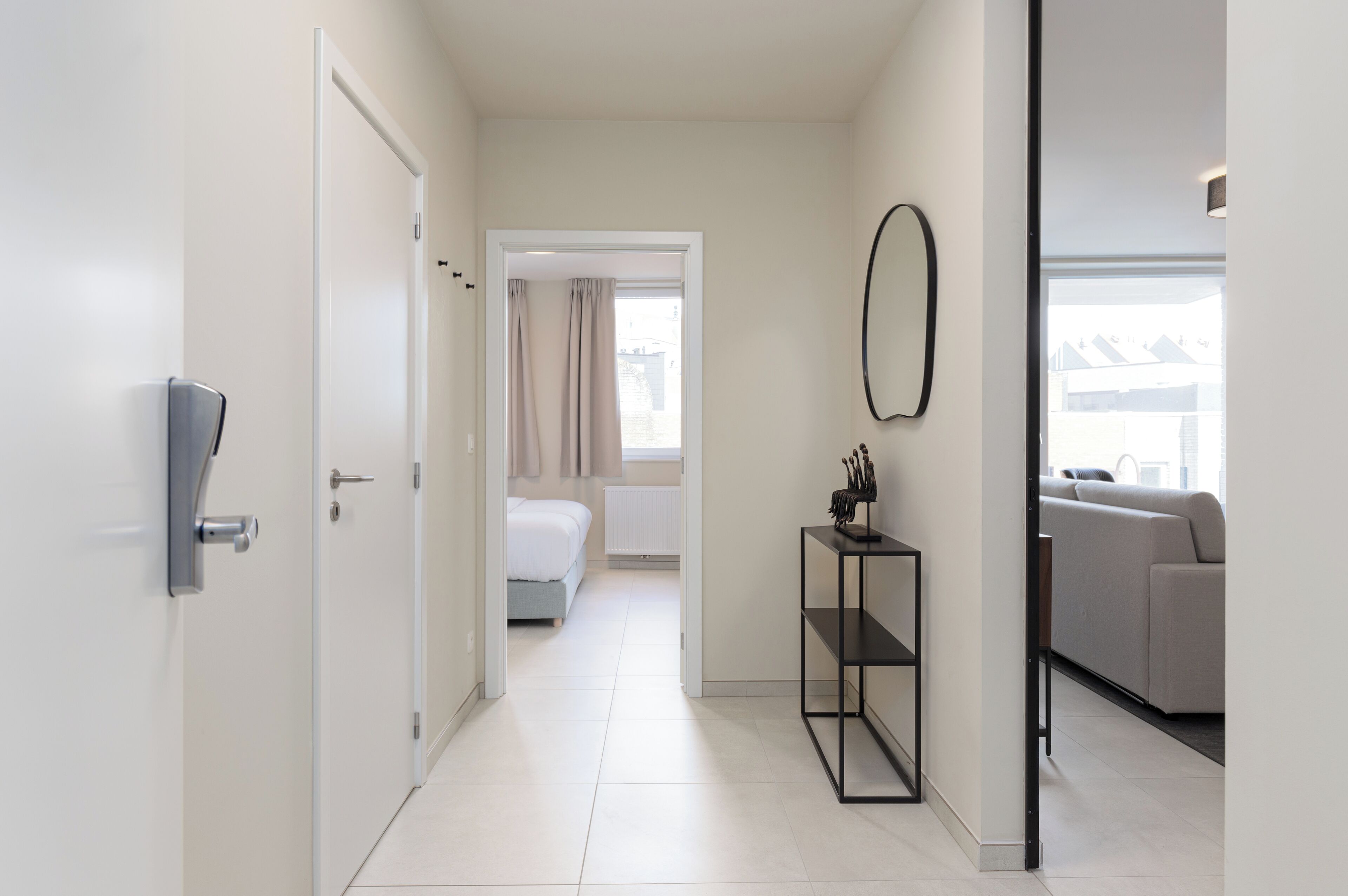 Un couloir d’hôtel moderne avec un lit, un canapé et une petite table sur laquelle se trouve un bloc à couteaux.