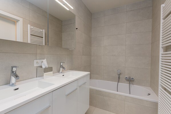 Un baño moderno con tocador doble, bañera y un espejo grande.