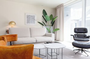 Un salon moderne comprenant un canapé, deux fauteuils, une table basse, un lampadaire et une grande plante.