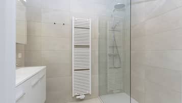 Et moderne badeværelse med et brusekabine i glas, en hvid radiator og en hvid vask.
