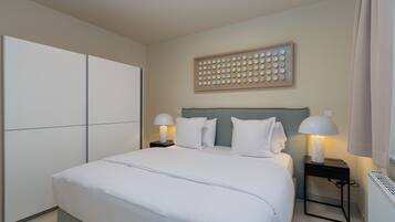 A neatly arranged bedroom with a large bed, two bedside tables with lamps, a wall-mounted artwork, and a radiator.