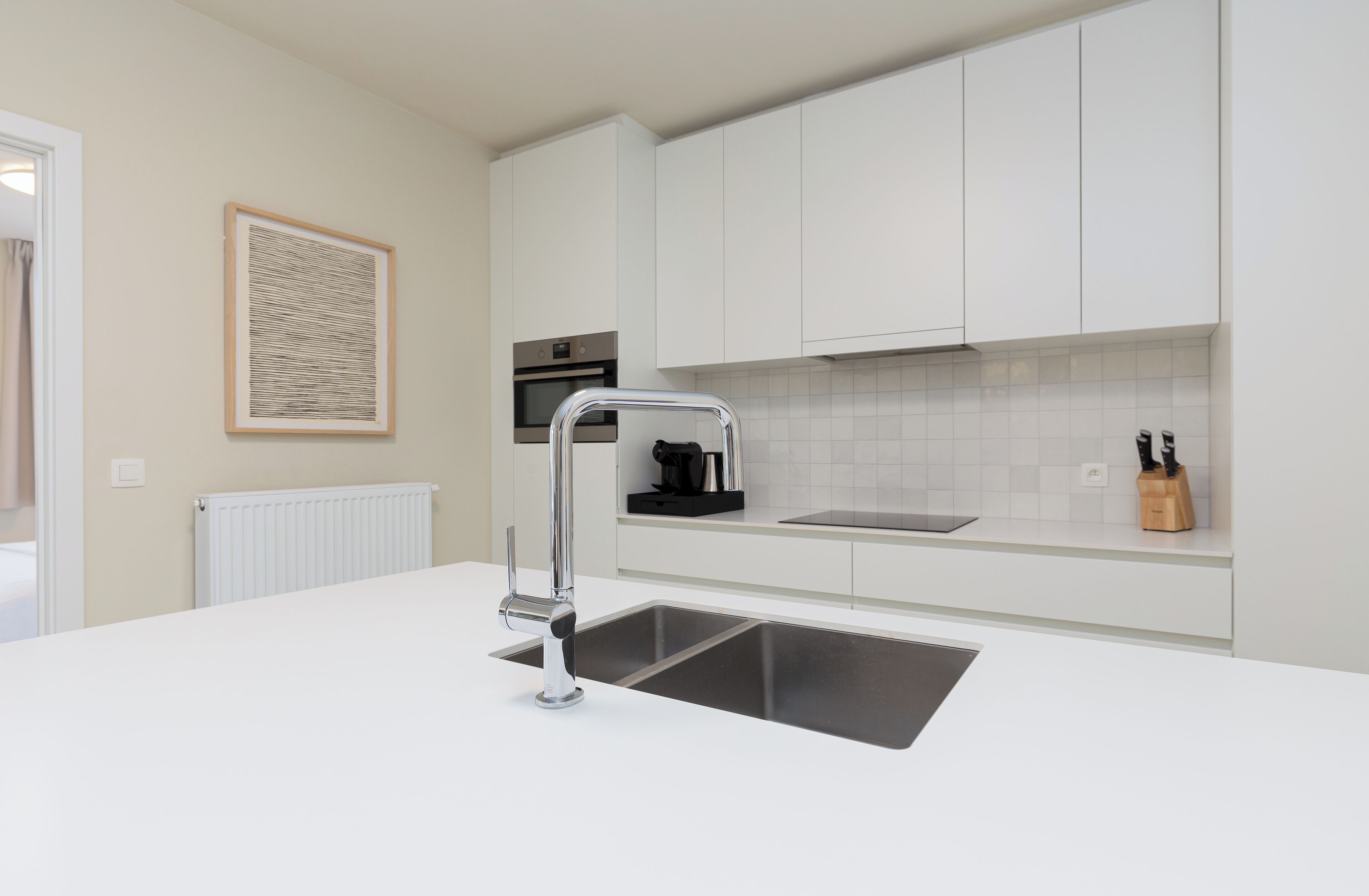 Una cocina moderna con armarios blancos, un lavamanos de acero inoxidable y un horno empotrado.