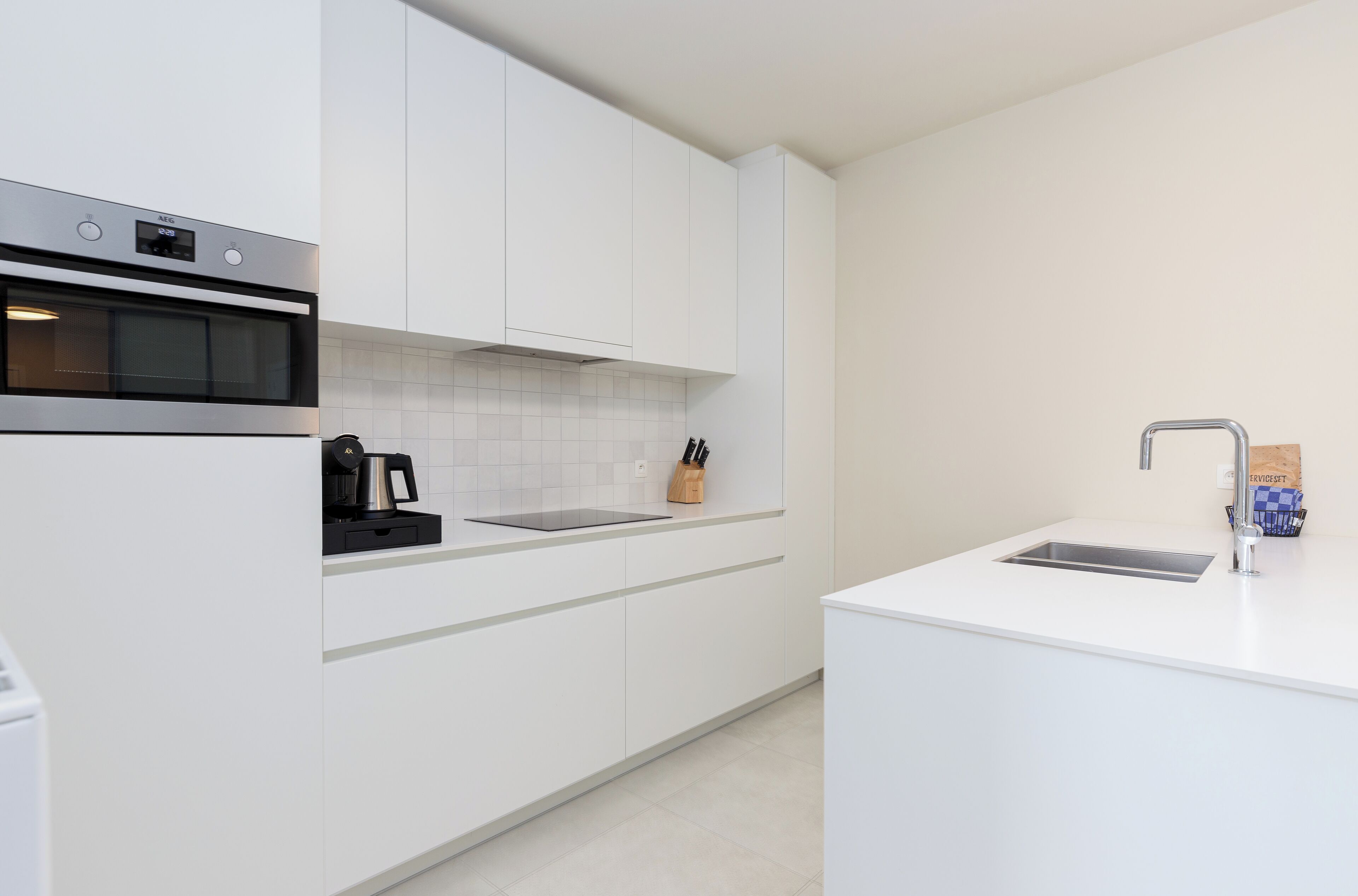 A modern kitchen with white cabinetry, a built-in oven, a coffee maker, and a sink.