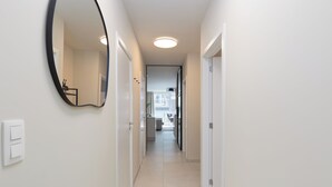 Een smalle gang met witte muren, een grote spiegel en een plafondlamp.