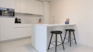 Een moderne keuken met witte kasten, een inbouwoven, een koffiezetapparaat en twee barkrukken.