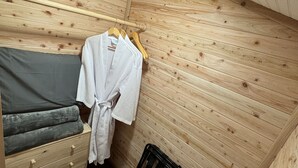 A small, cozy room with wooden walls, a bed with gray bedding, a wooden dresser, and a hanging rack with clothes. - Zen Den - jetted tub, massage chair, home theater, EV charger, King bed, parking (Burleson)