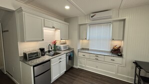 A kitchen with white cabinetry, a granite countertop, a built-in microwave, and a window with blinds. - Zen Den - jetted tub, massage chair, home theater, EV charger, King bed, parking (Burleson)