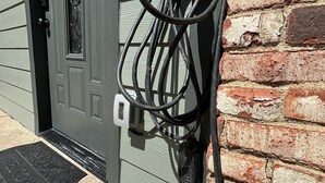 A power outlet with a charging cable plugged in, a door with a window, and a brick wall. - Zen Den - jetted tub, massage chair, home theater, EV charger, King bed, parking (Burleson)