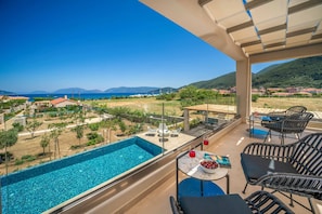 A balcony with a pool, outdoor seating, and a view of the sea and mountains. - Villa Claire Sami (Kefalonia)