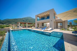 A modern two-story house with a swimming pool, outdoor seating, and a view of the mountains. - Villa Claire Sami (Kefalonia)