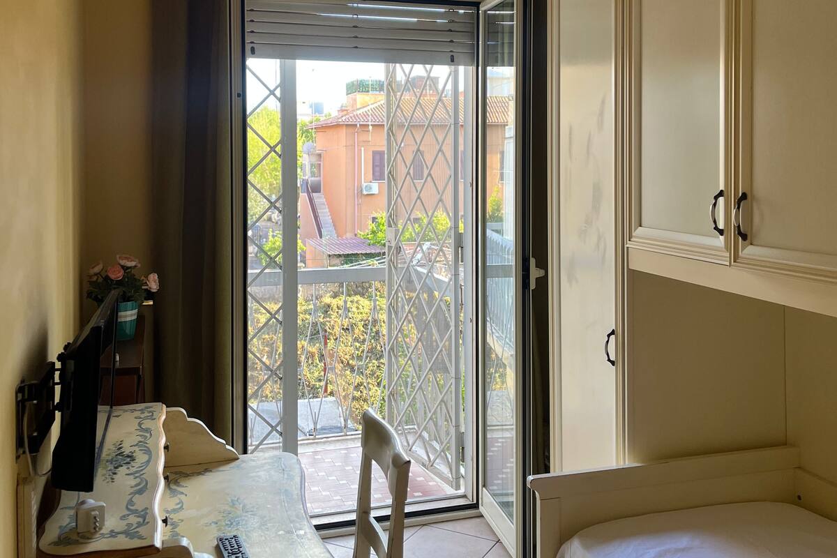 A room with a bed, a table with a chair, a small desk, and a window with curtains.