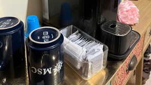 A coffee machine, a stack of blue cups, and a container with sachets on a counter. - Specter Guesthouse (Nettuno)