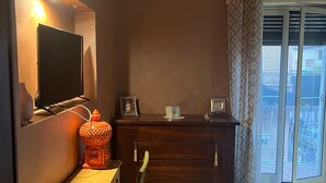 A bedroom with a bed, a desk with a chair, a television, a dresser, and a window with curtains. - Specter Guesthouse (Nettuno)