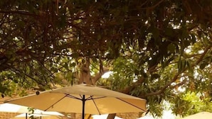 Un espace extérieur aménagé en terrasse, avec des tables et des chaises rondes, entouré de murs en briques et protégé par des parasols.