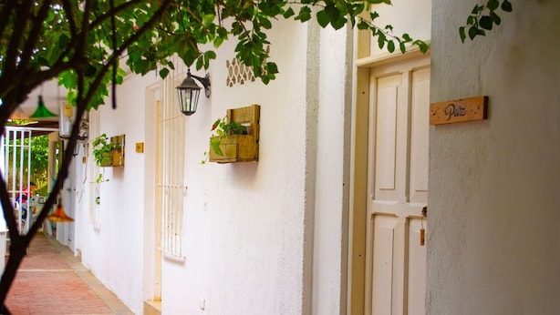 Un couloir étroit aux murs blancs, une porte en bois portant l’inscription « Plaza », et un petit bac à fleurs en bois contenant une plante.