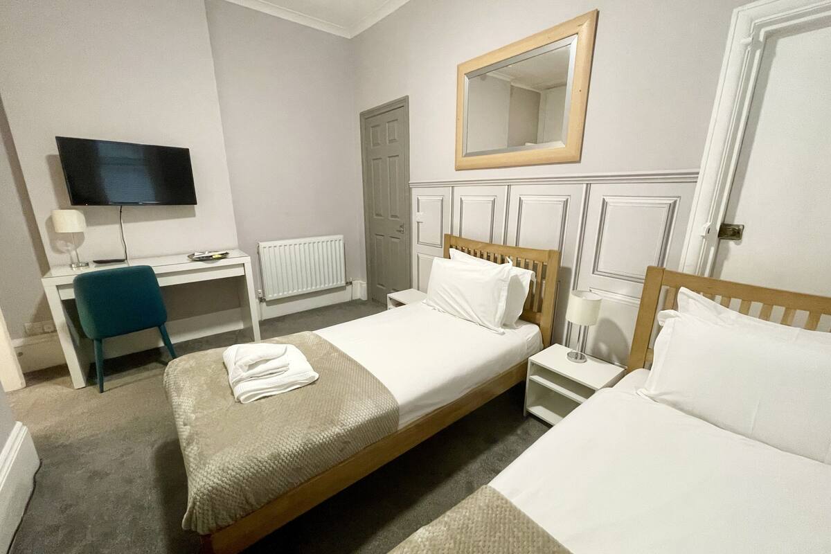 A hotel room with a bed, a desk, a chair, a television, and a mirror.