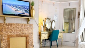 A living room with a television, a fireplace, a glass coffee table, a blue chair, and a mirror. - The X Hotel (Hove)