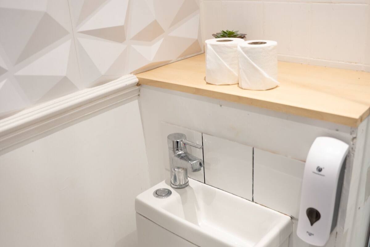A modern bathroom with a toilet, sink, and a shelf with toilet paper and a small plant.