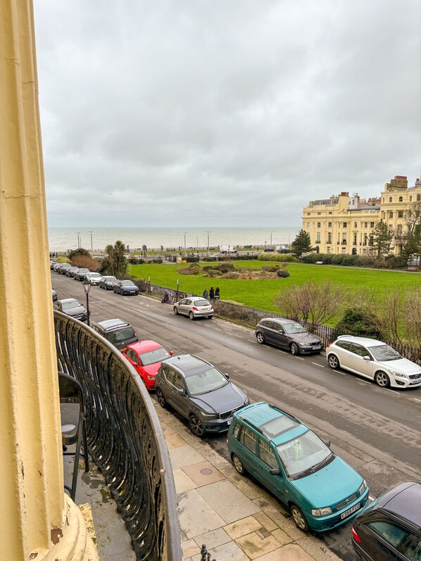 Vista de la calle con coches estacionados, un edificio de arquitectura clásica y vista al mar.