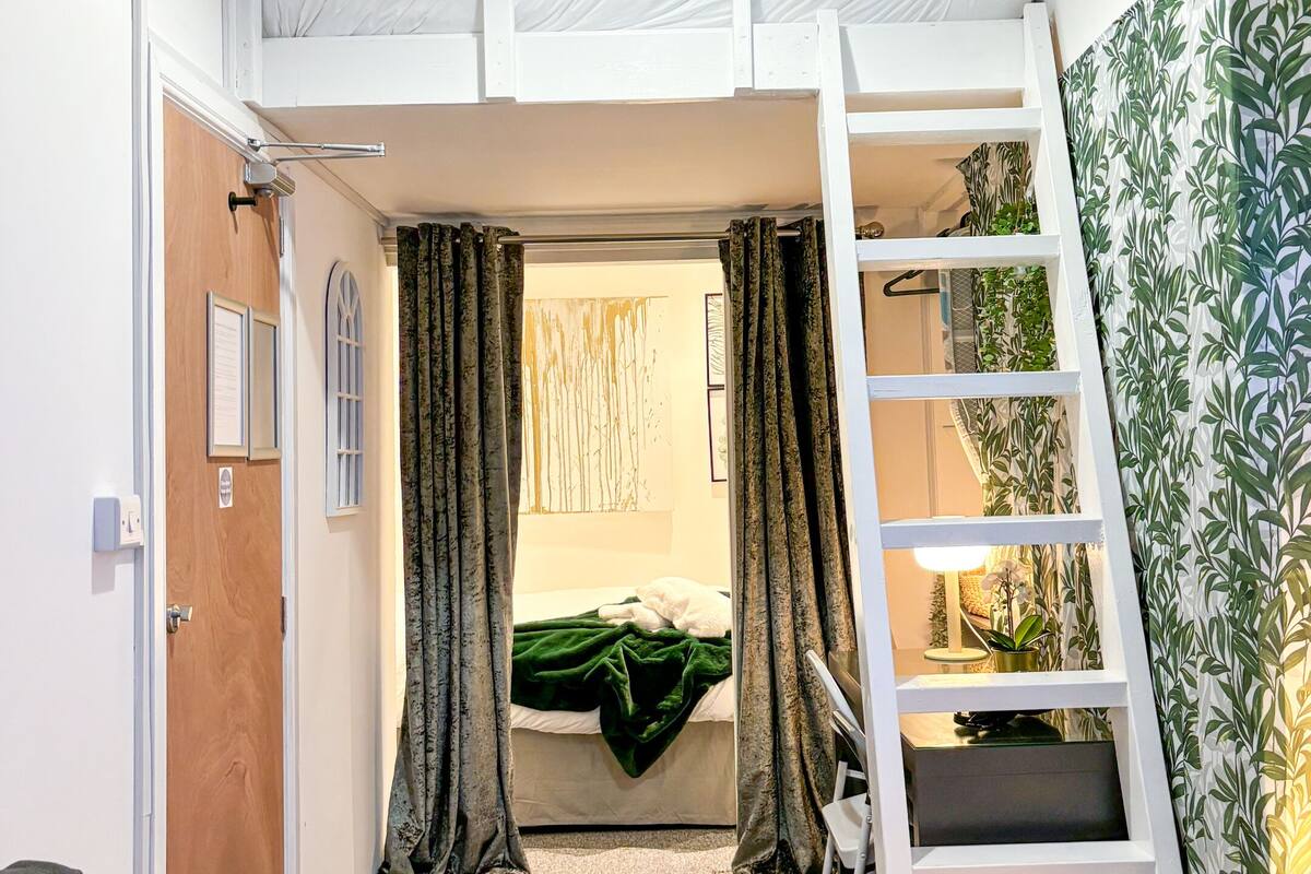 A compact room with bunk beds, a ladder, a door, and a small desk with a lamp.