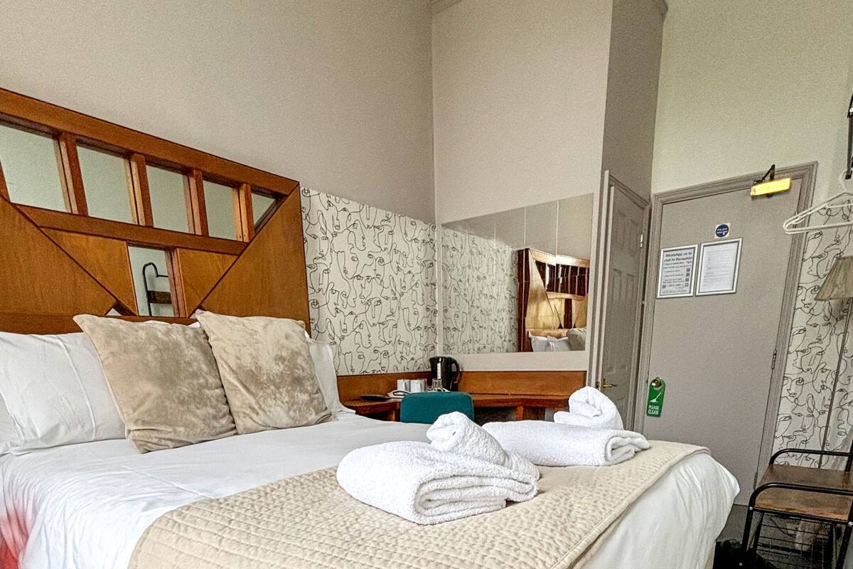 A hotel room with a bed, a bedside table, a mirror, and a door with a sign.