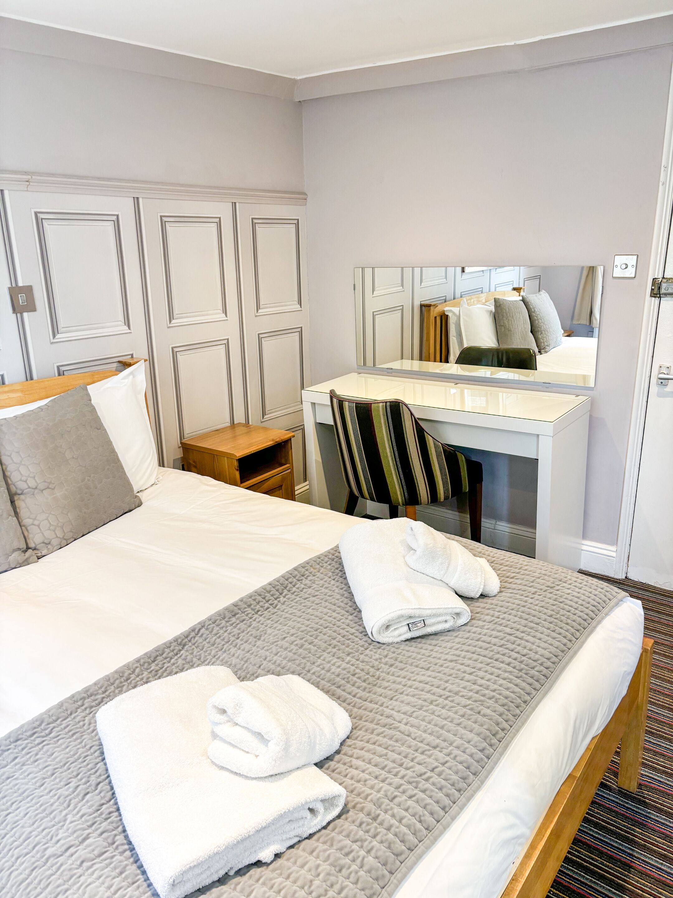 A hotel room with a bed, a desk, a chair, and a mirror.