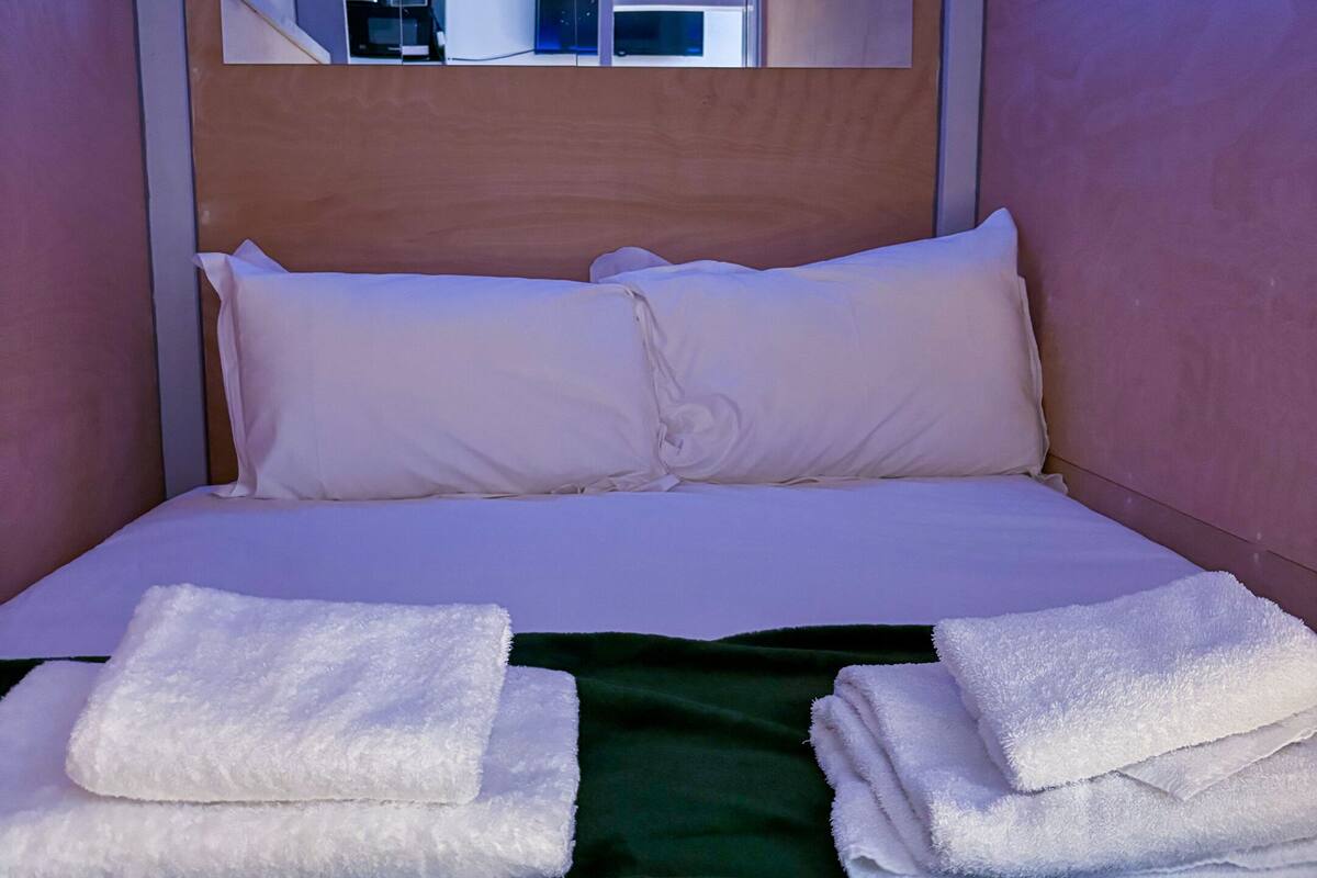 A single bed with white linens and two folded towels, a green throw blanket, and a wooden headboard.