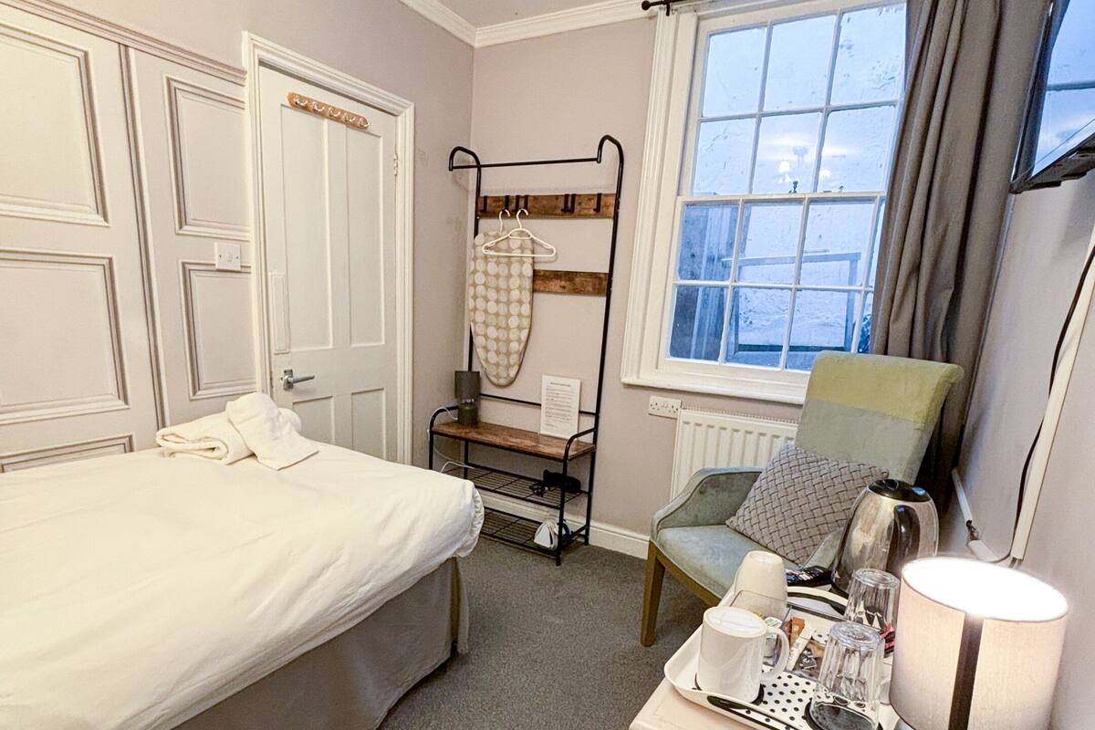 A hotel room with a bed, a chair, a table with a lamp, and a window with curtains.