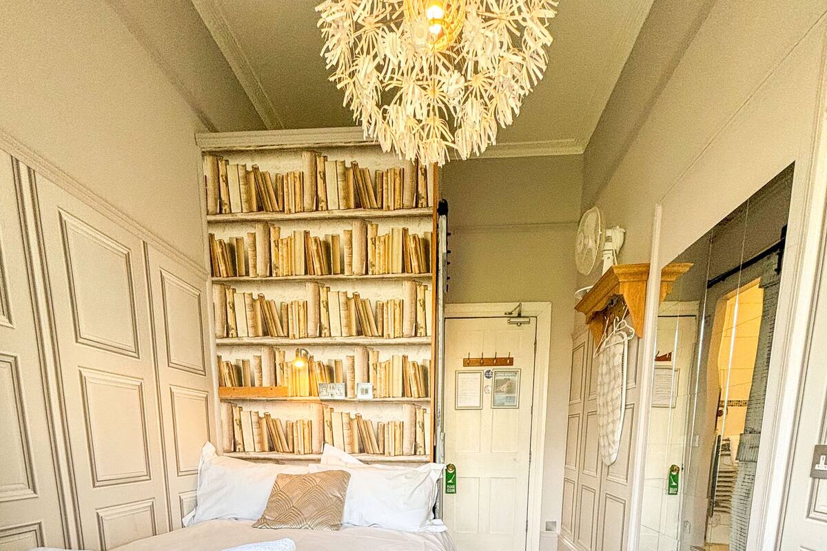 A hotel room with a large bed, a bookshelf, a mirror, and a wardrobe.