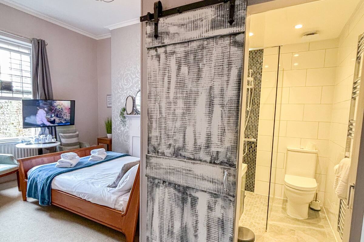A bedroom with a bed, a TV, a sliding door to a bathroom, and a chandelier.