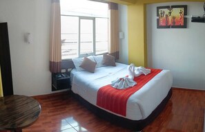 Quarto de hotel com cama, mesa de cabeceira, mesa e janela com cortinas.