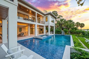 Enjoy a serene atmosphere in our garden, surrounded by lush greenery and palm trees, with a spacious outdoor pool and large windows.