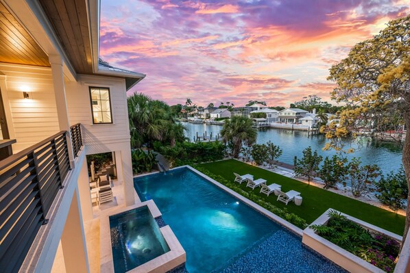 Relax by the pool surrounded by lush greenery and a serene body of water.