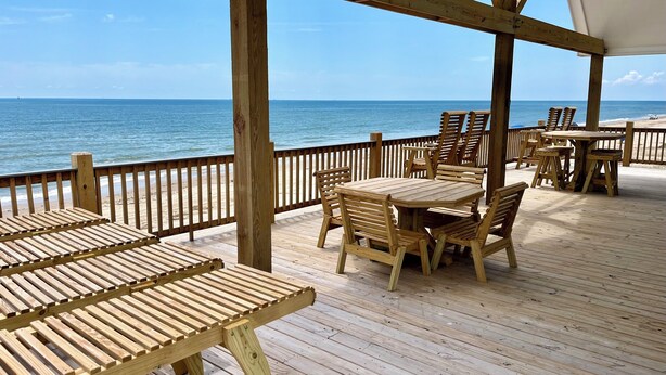 Een houten terras met tafels en stoelen, met uitzicht op een strand.
