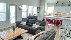 Een ruime woonkamer met een grijze modulaire bank, een houten salontafel en een plafondventilator.