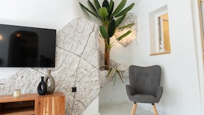 A modern living room with a stone accent wall, a flat-screen TV, a grey armchair, and a wooden coffee table. - White Occhio Villa Santorini (Santorini)